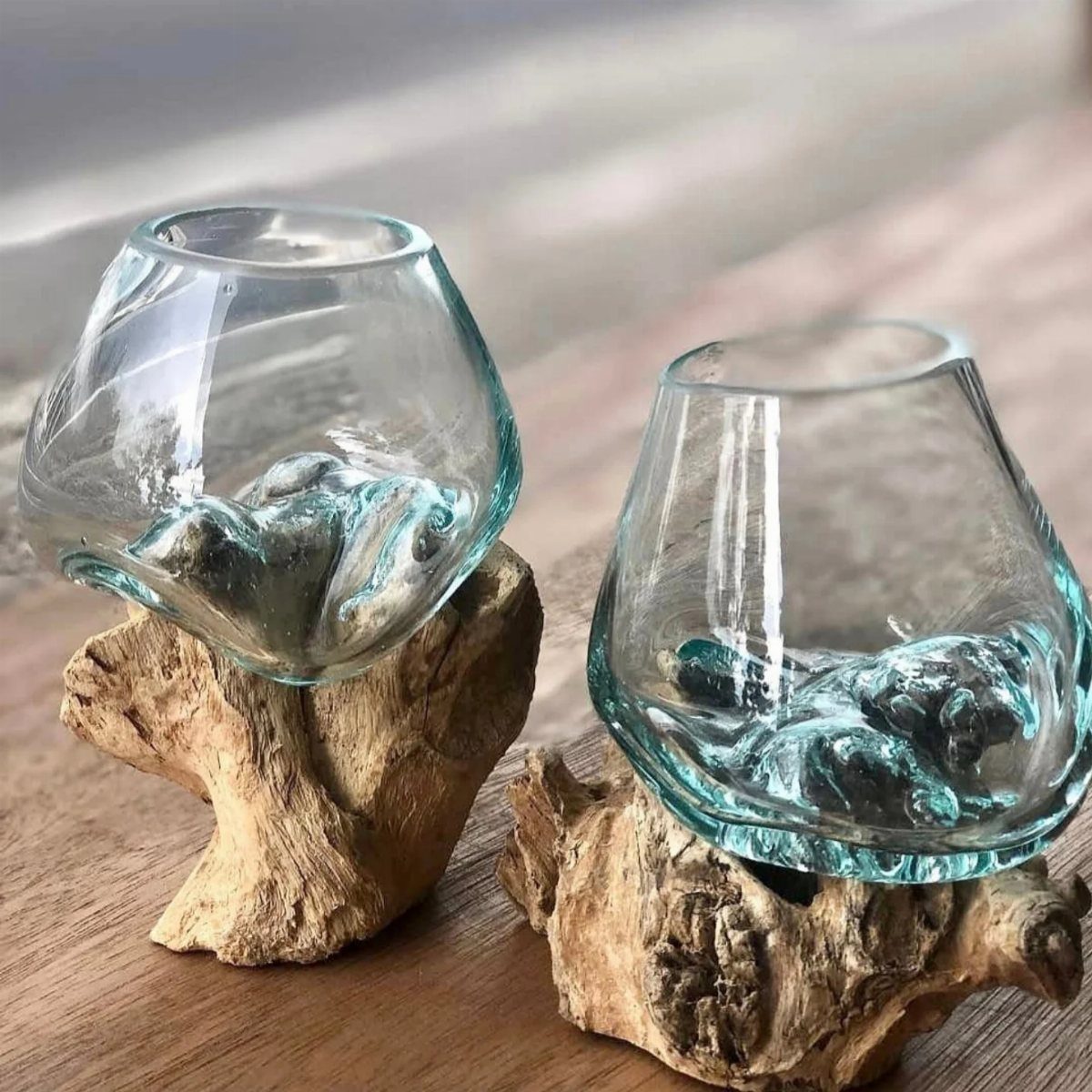 Clear glass vessels resting on natural driftwood pieces on a wooden surface.