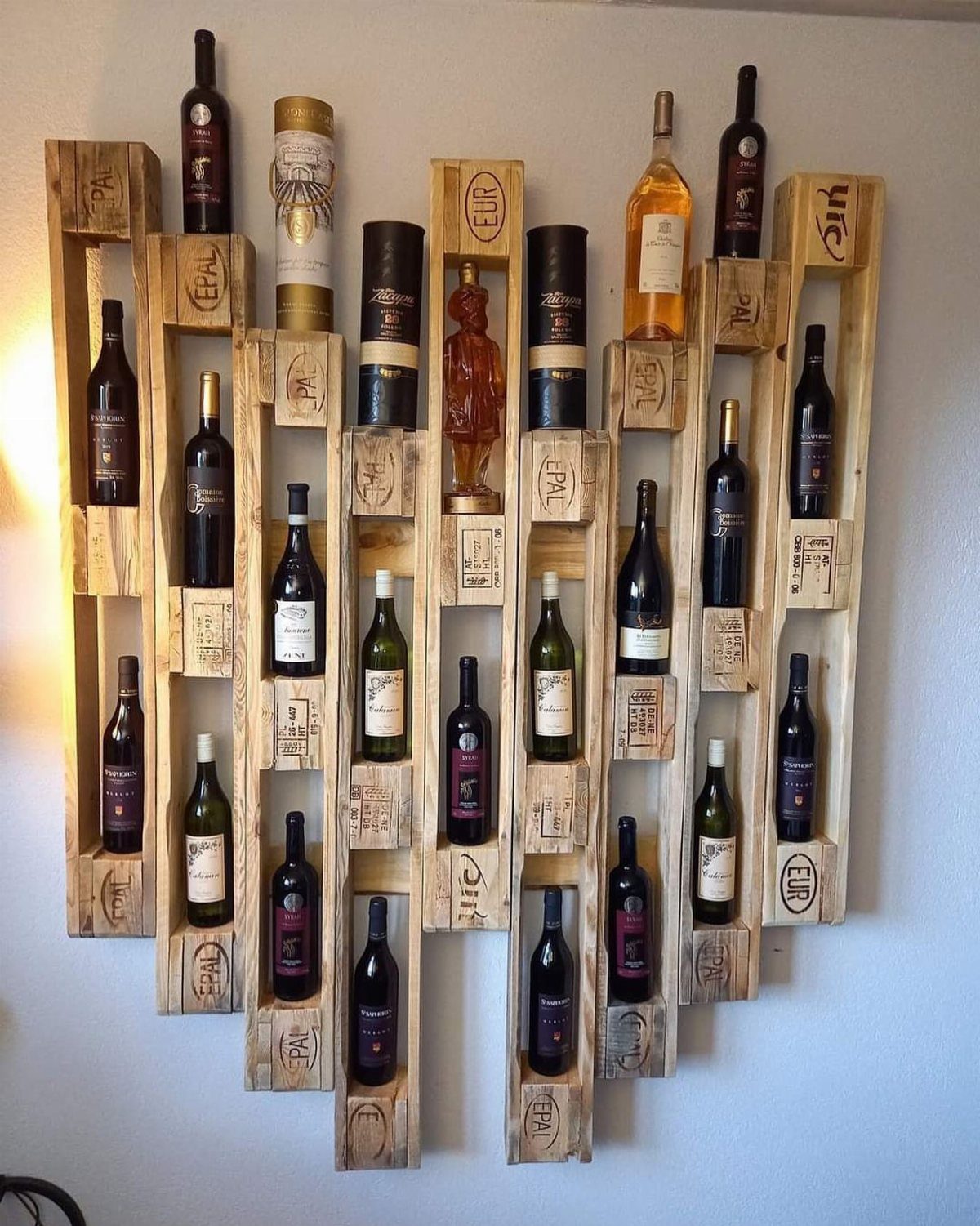 Pallet wood wine rack mounted on a white wall holding several wine bottles.