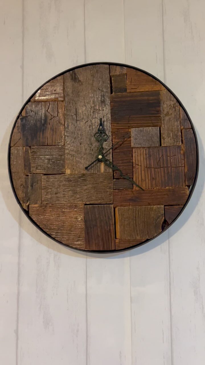 Round wooden clock made of reclaimed planks hanging on a white paneled wall.
