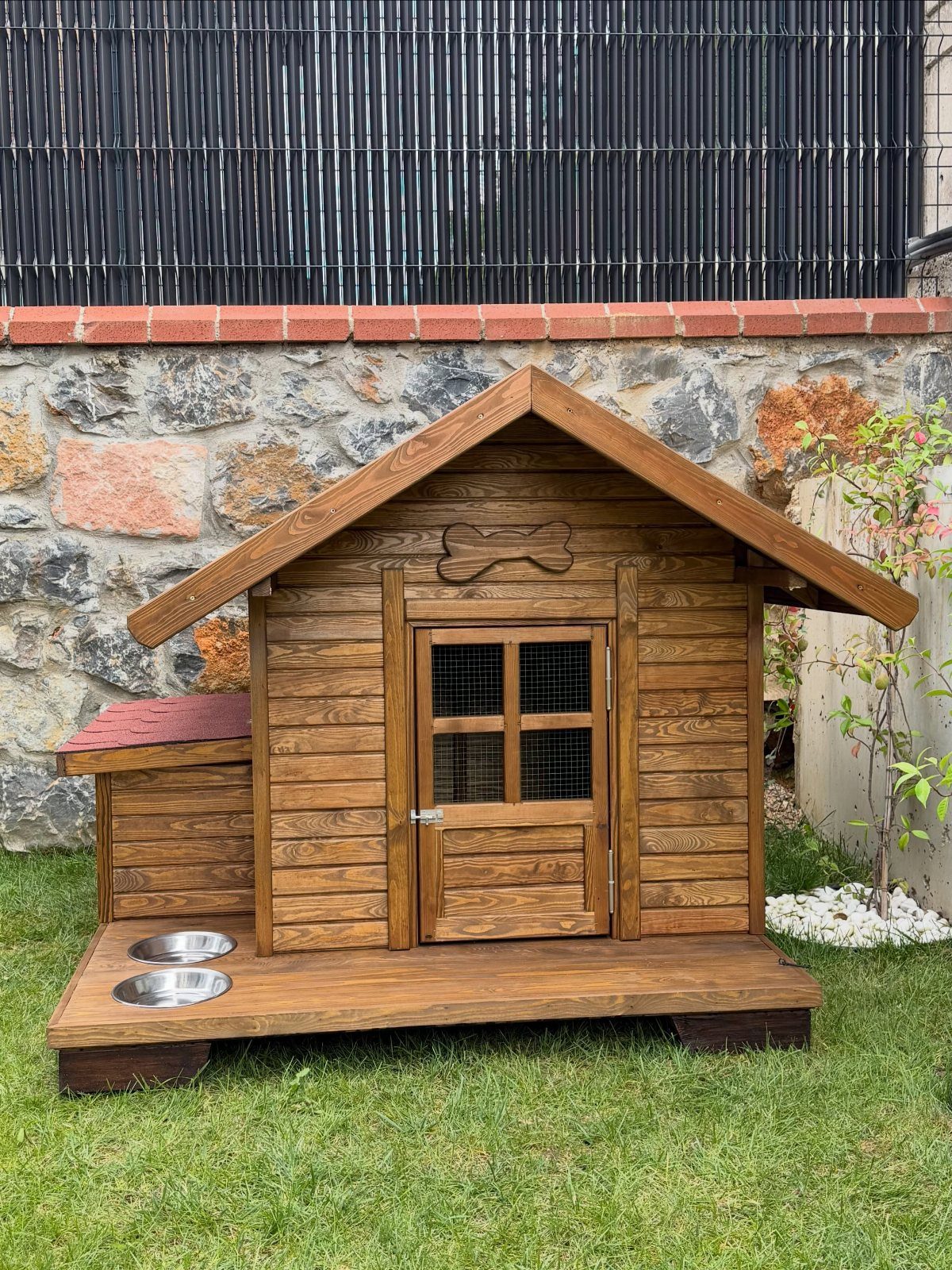 Wooden dog house with a porch and food bowls on a green lawn.