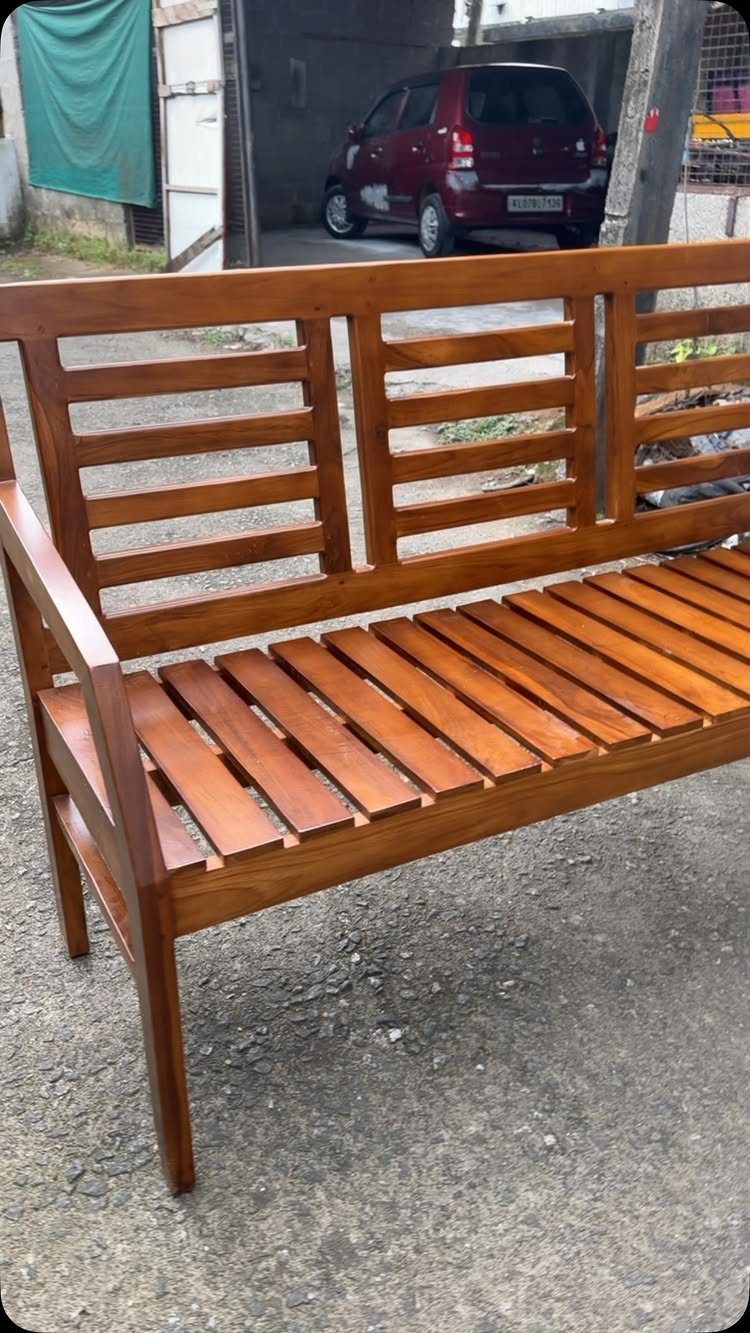 Polished brown wooden bench with slatted backrest and seat on concrete ground.
