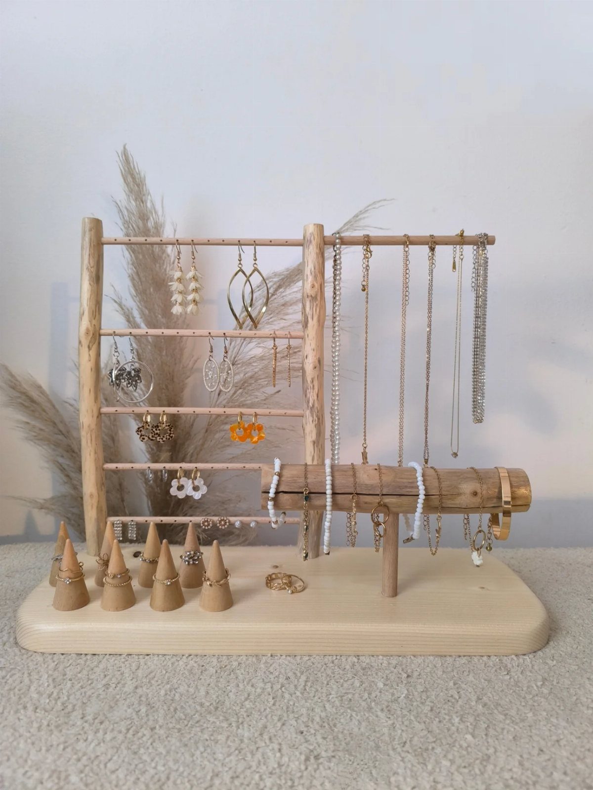 Wooden jewelry organizer holding gold earrings, necklaces, and rings on a light base.