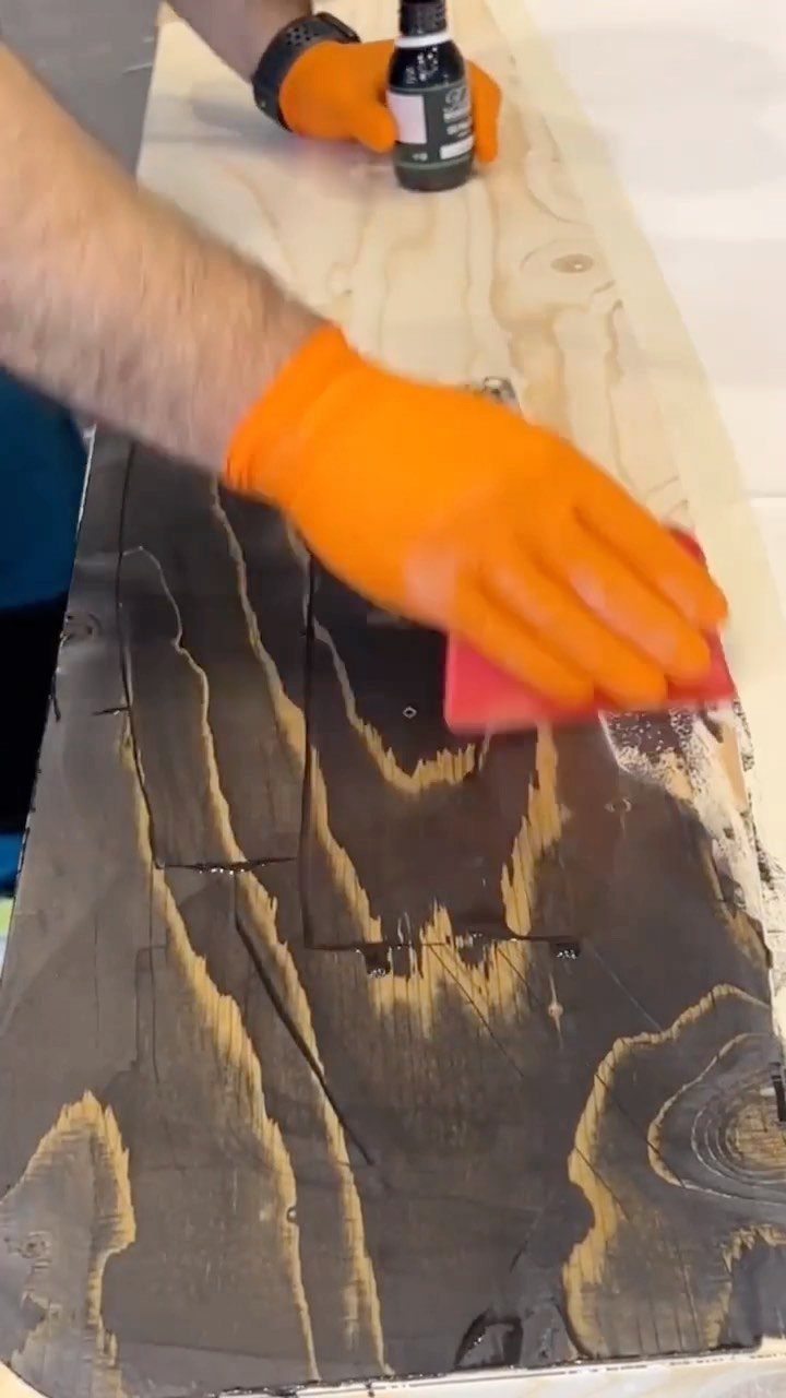 Person applying dark wood stain to a light wooden board with a red rag