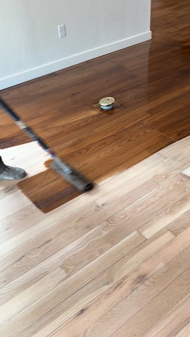 Wood Grain Stain: 8 Ideas for Color and Application 7 Person applying dark brown stain to light hardwood floor planks with a long applicator.