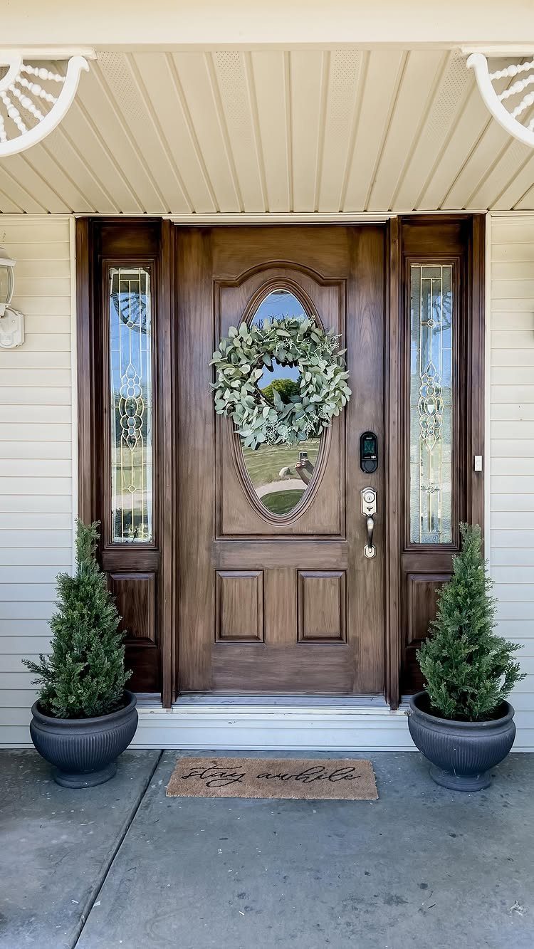 Wood Grain Stain: 8 Ideas for Color and Application 1 Dark brown stained wooden front door with a green wreath and potted shrubs.