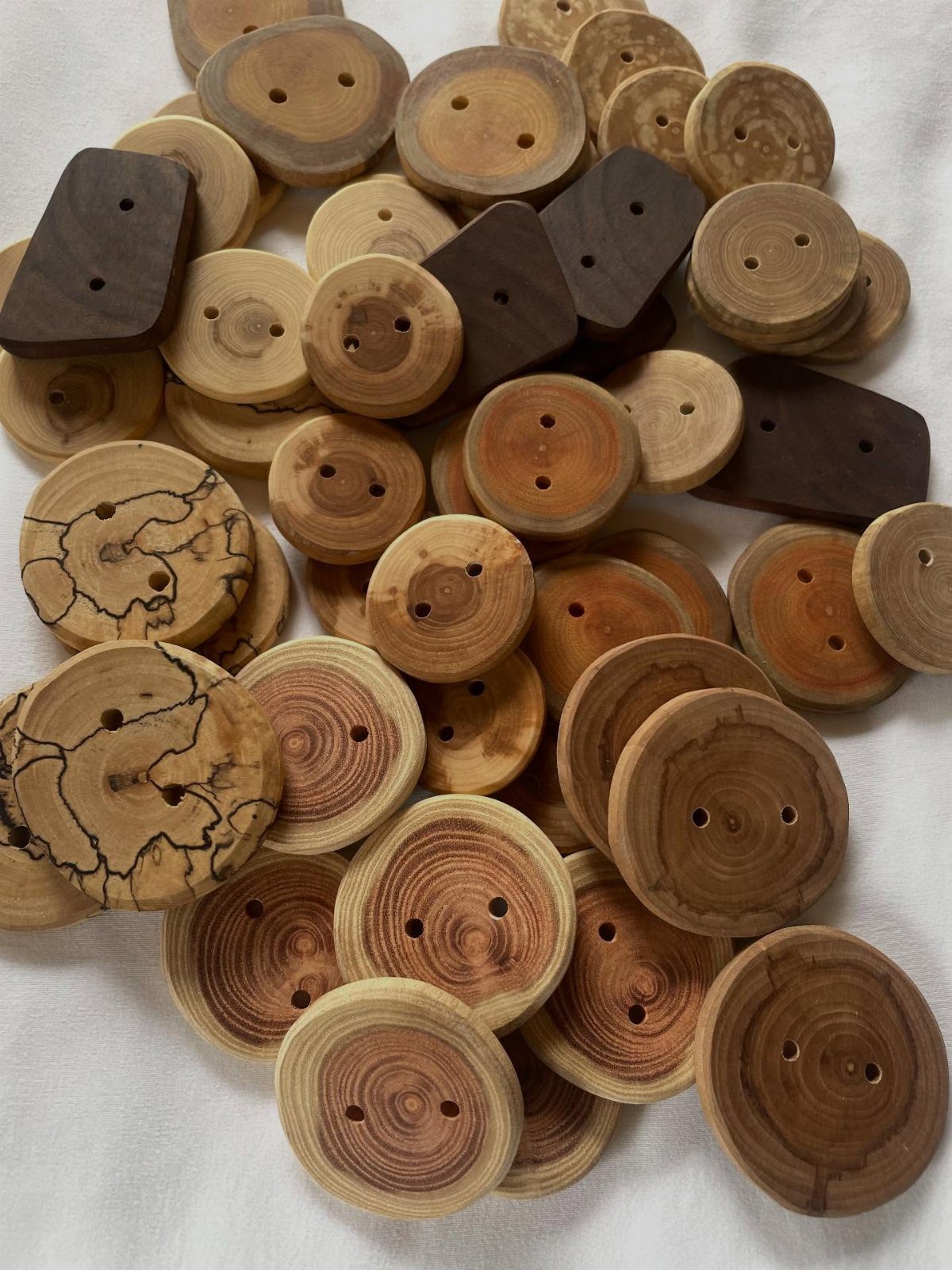 10 Wood Slice Crafts for Home Decor, Gifts and Games 3 Small circular wooden buttons made from wood slices scattered on white fabric.