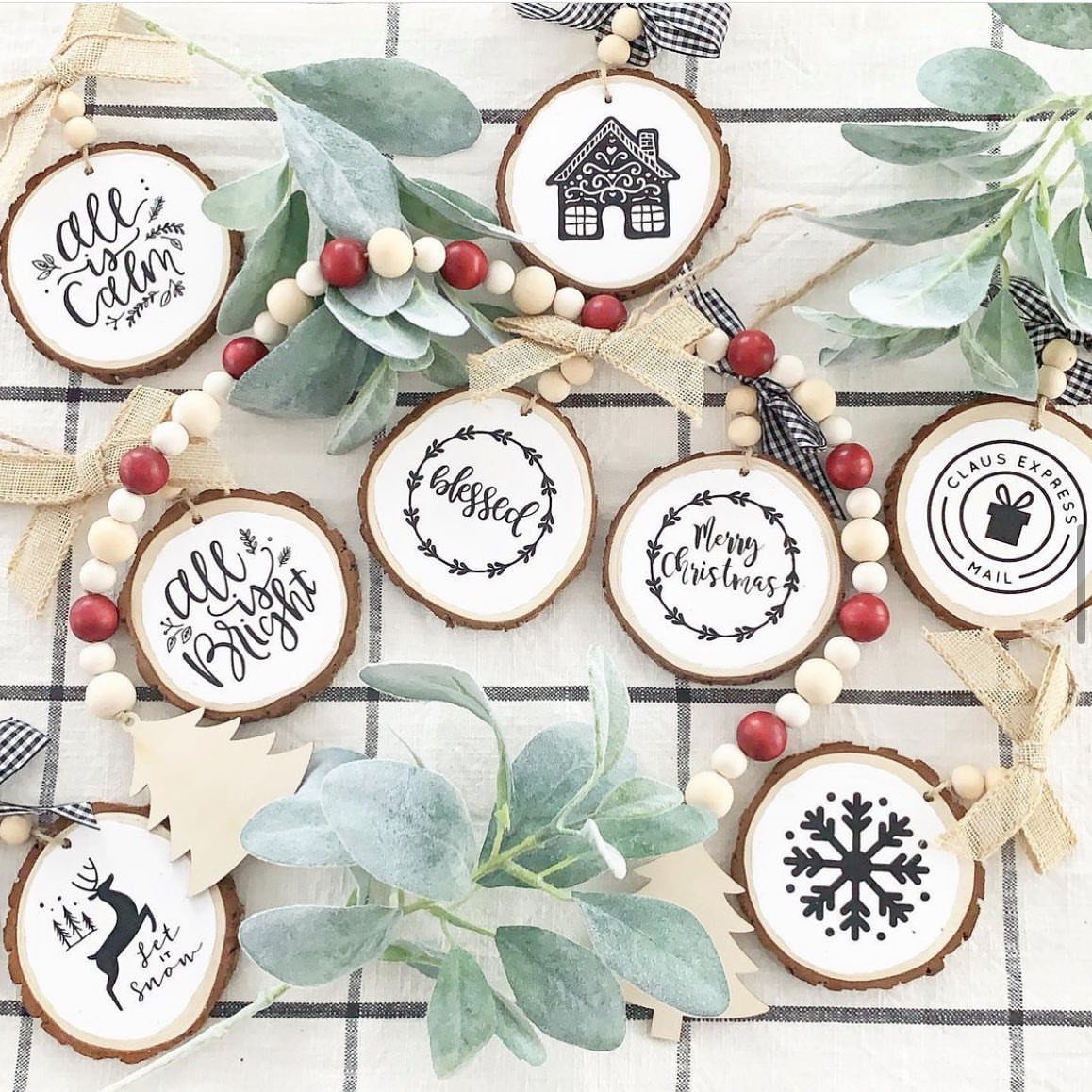10 Wood Slice Crafts for Home Decor, Gifts and Games 5 Hand-painted wood slice ornaments with holiday designs and text arranged with festive greenery.