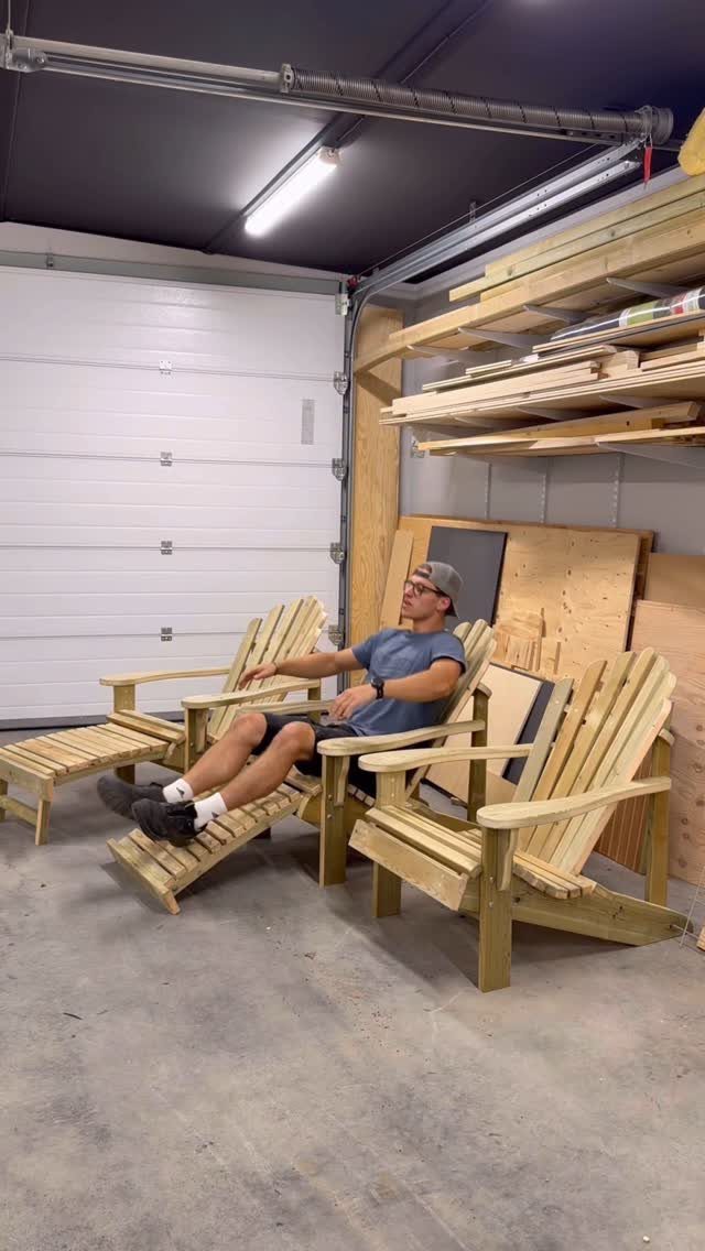 Three light-colored wooden Adirondack chairs in a garage with a man sitting in one.