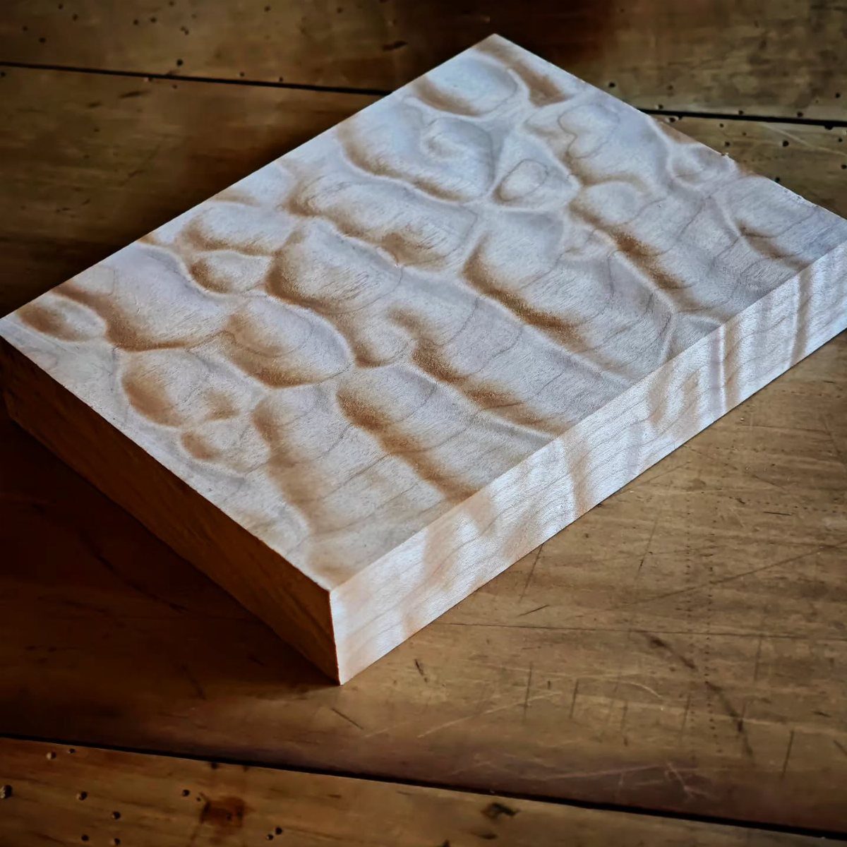 Carved wooden block with organic wave patterns resting on a wooden surface