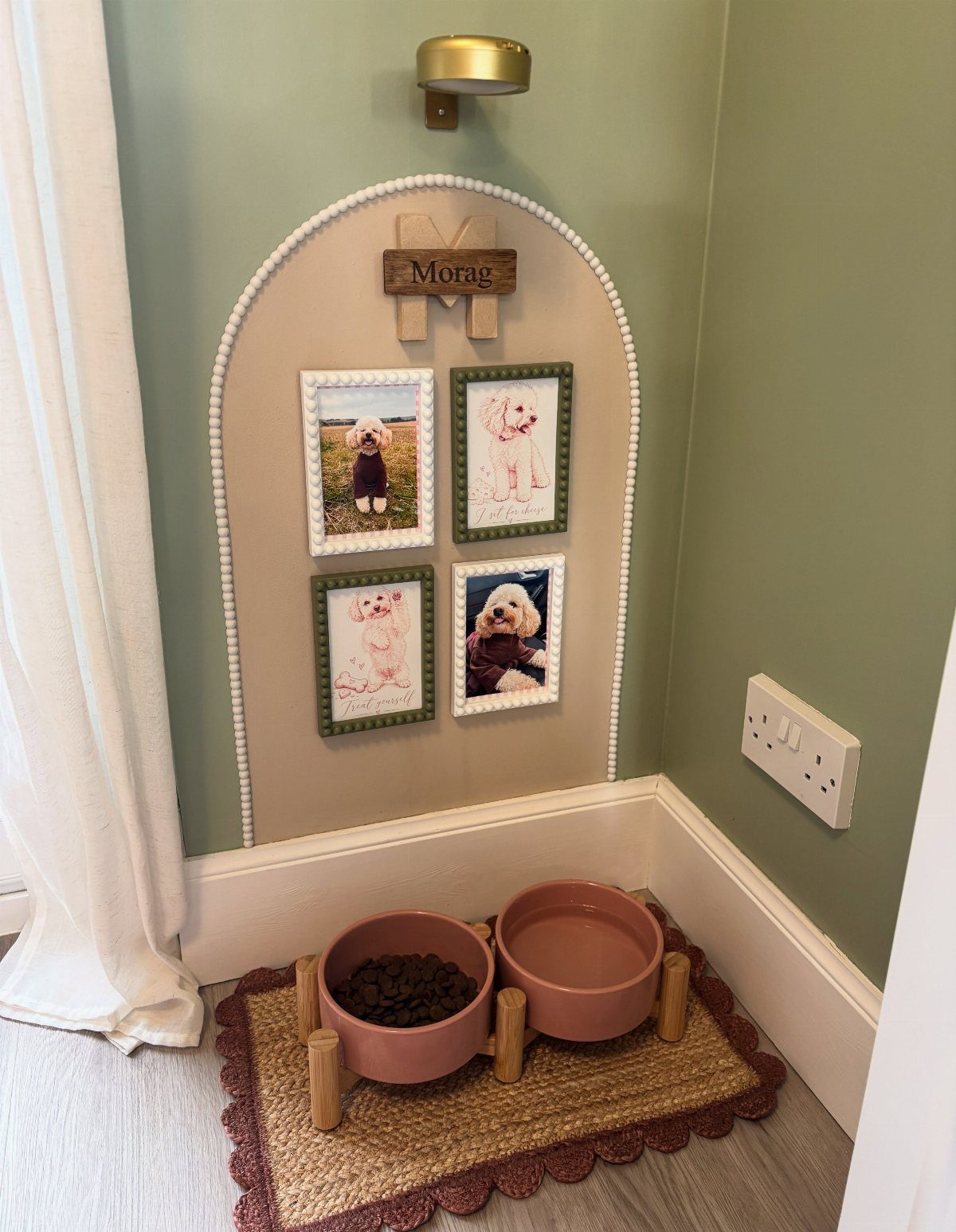 Raised wooden dog feeding station with two pink bowls on a woven mat.
