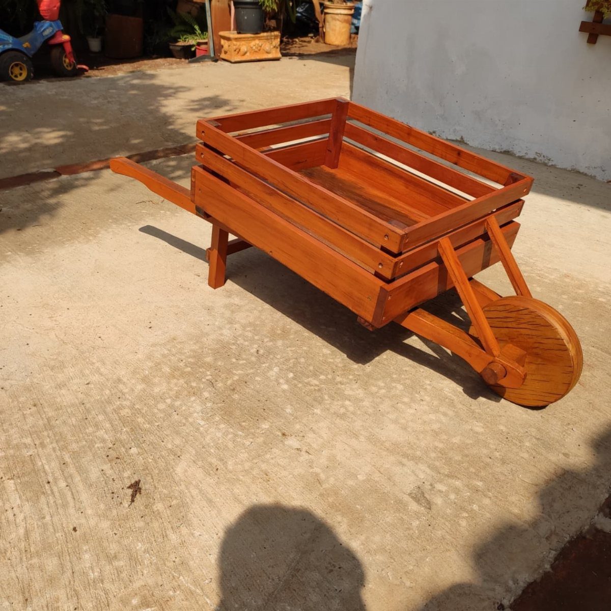 Wooden cart with a slatted bed and a single large wheel on concrete.