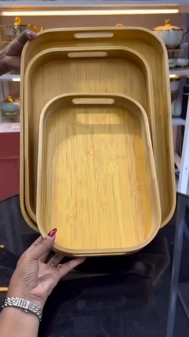 Three nested light wood trays with rounded corners and handle cutouts.