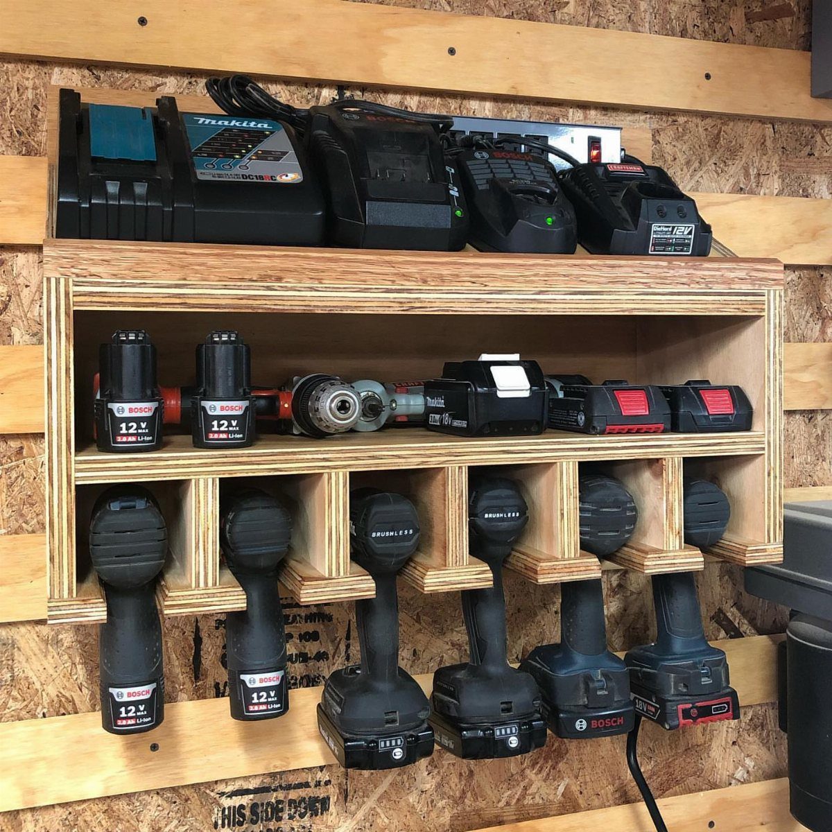 Wooden power tool charging station holding cordless drills and batteries on a wall.