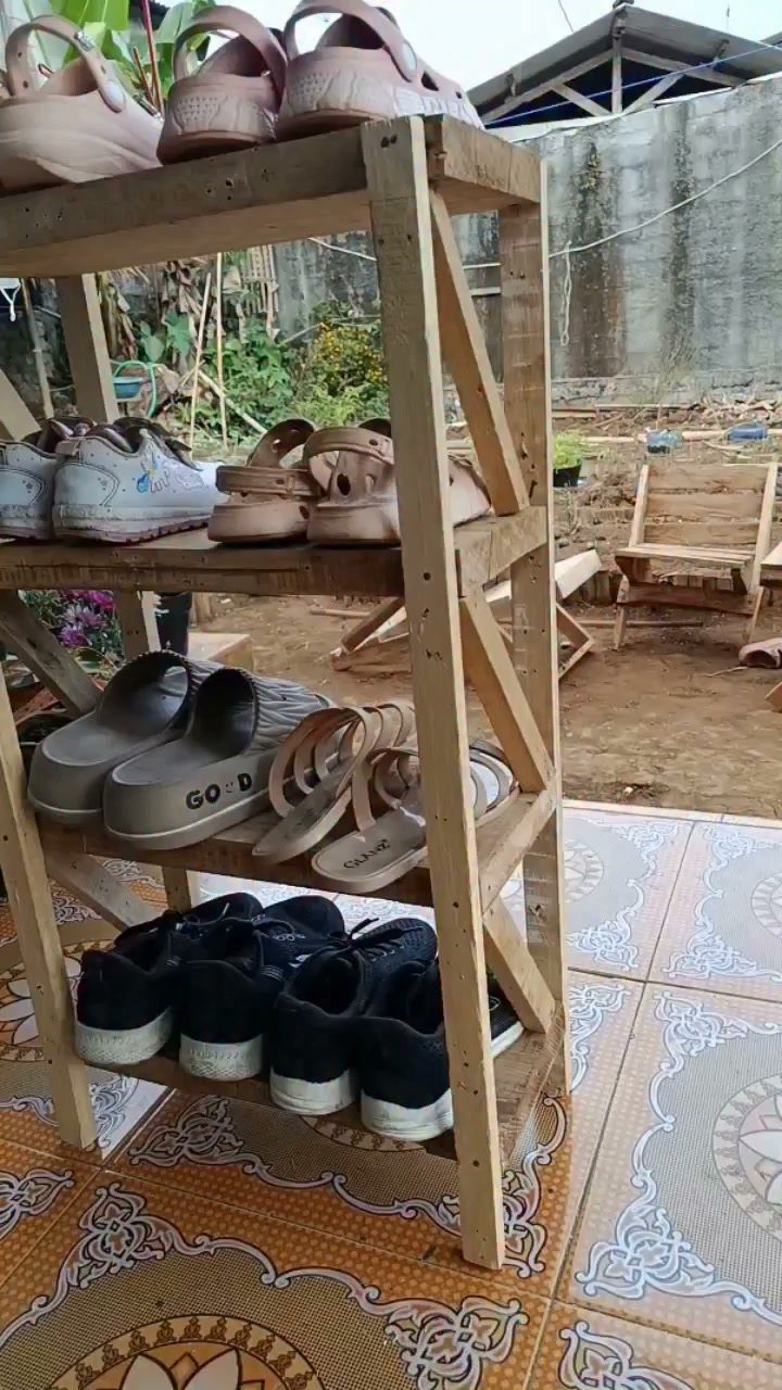 Wooden four-tier shoe rack holding various footwear on a patterned tile floor outdoors.