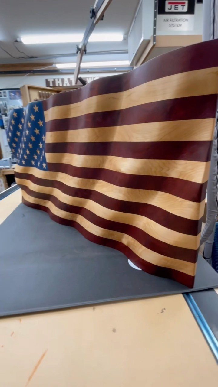 Carved wooden American flag sculpture with a waving effect in a workshop.