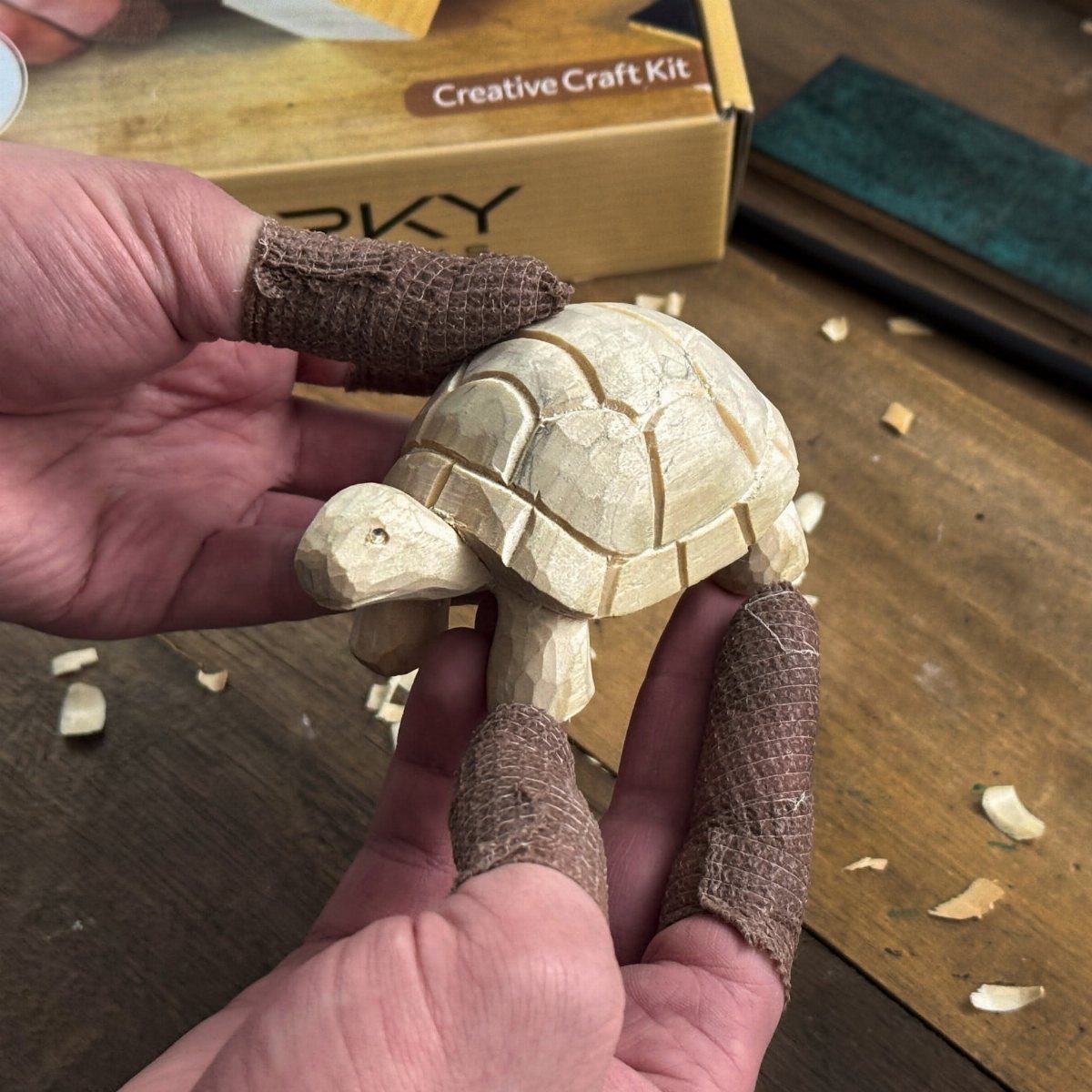 Hand-carved wooden turtle held by a person over a wooden table with shavings.