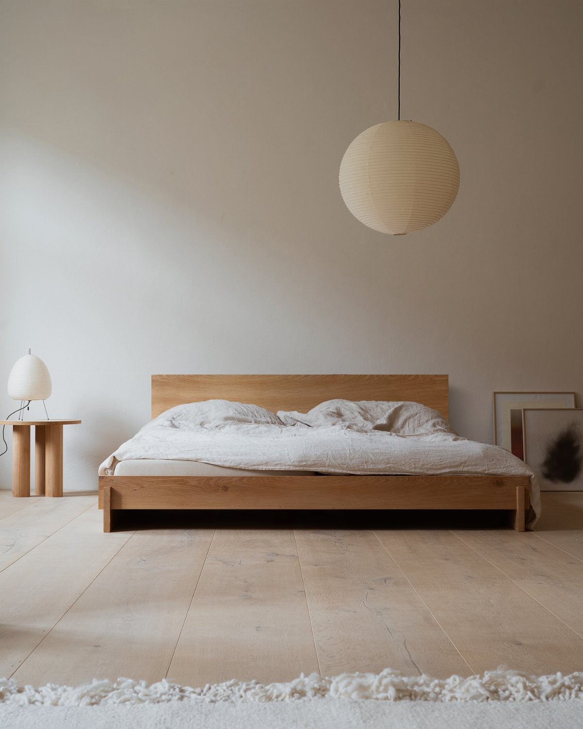 Solid wood bed frame with white bedding in a minimalist, brightly lit bedroom