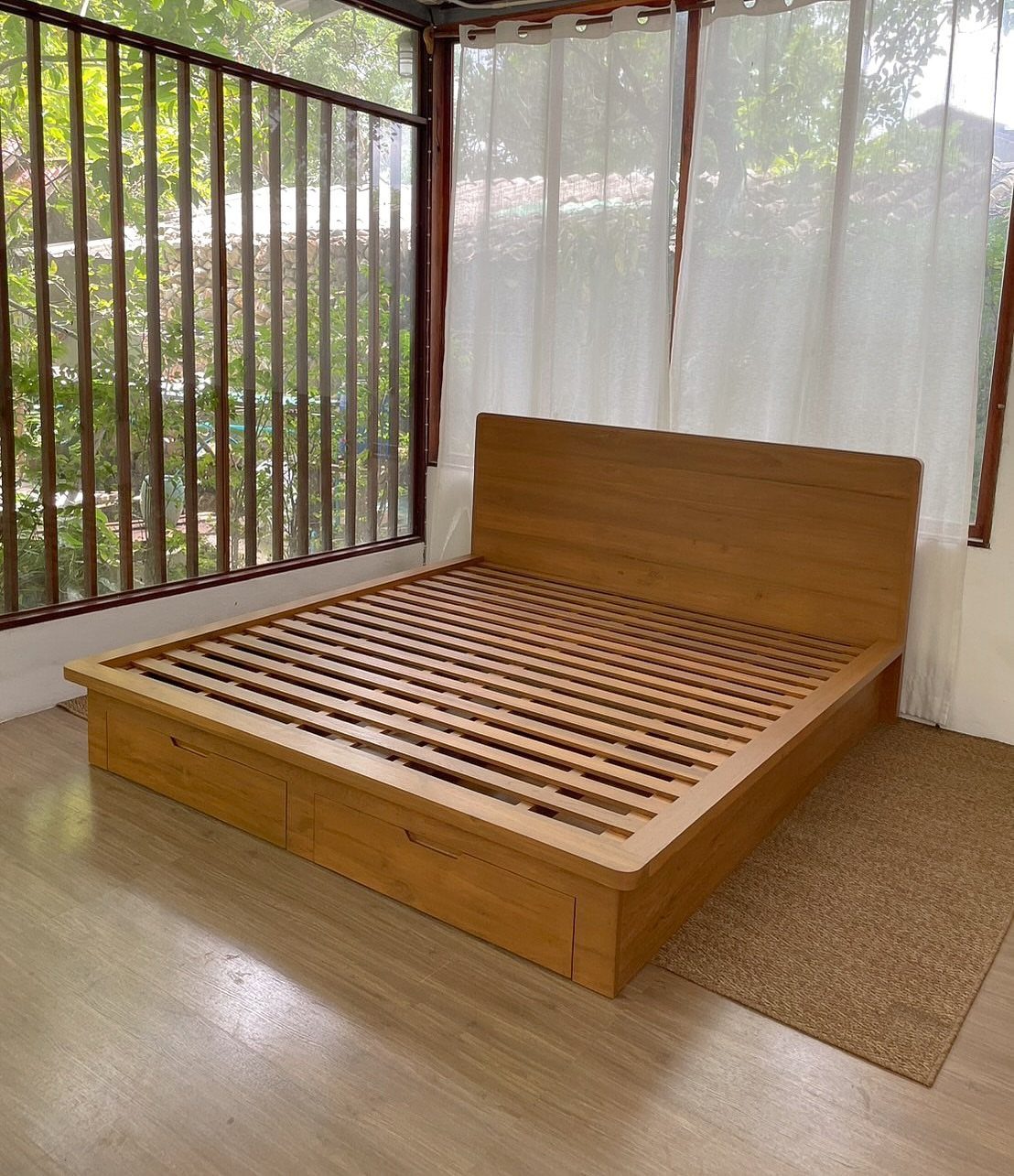 Solid wood bed frame with headboard and under-bed drawers in a bright room.