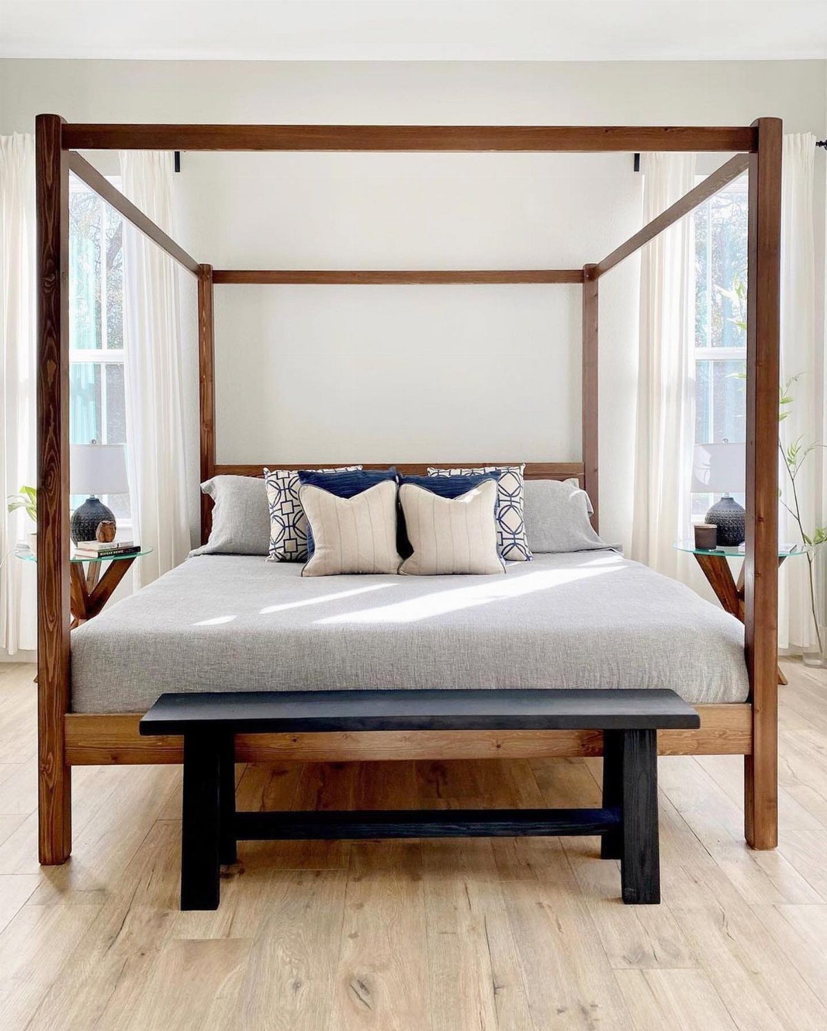 Wooden four poster bed frame with grey bedding and a black bench in bedroom