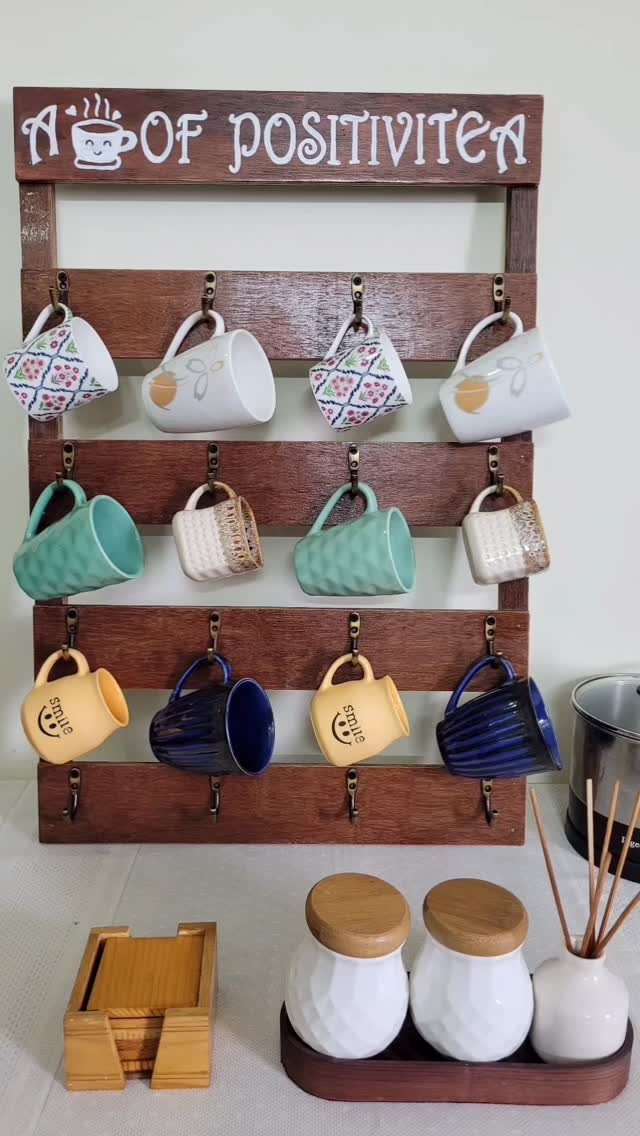 Wooden wall-mounted coffee cup holder with colorful mugs and positivity quote.