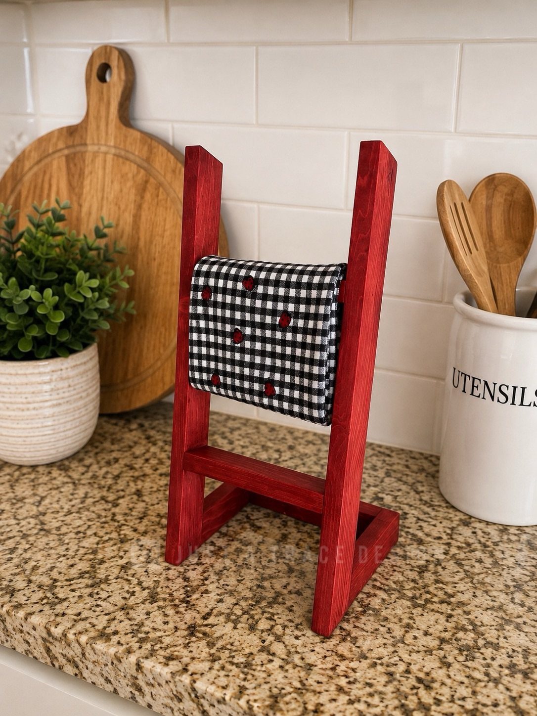 Red wooden towel rack holding a checkered cloth on a granite kitchen counter.