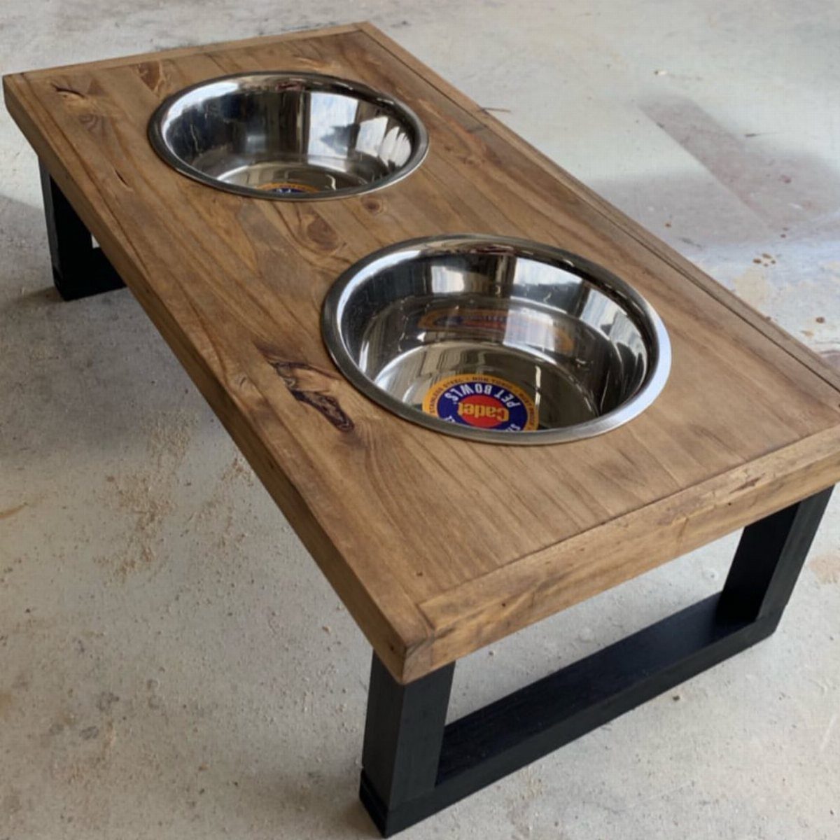 Wooden raised dog bowl stand with two stainless steel bowls and black metal legs.