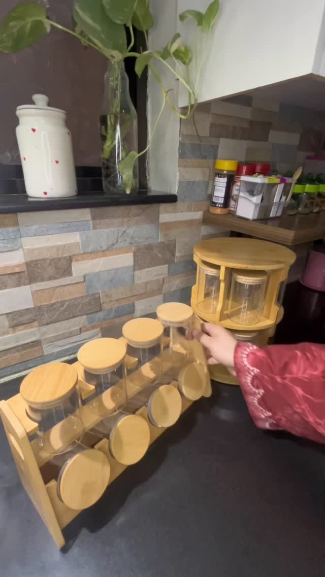 Wooden spice rack holding glass jars with lids on a black kitchen countertop.