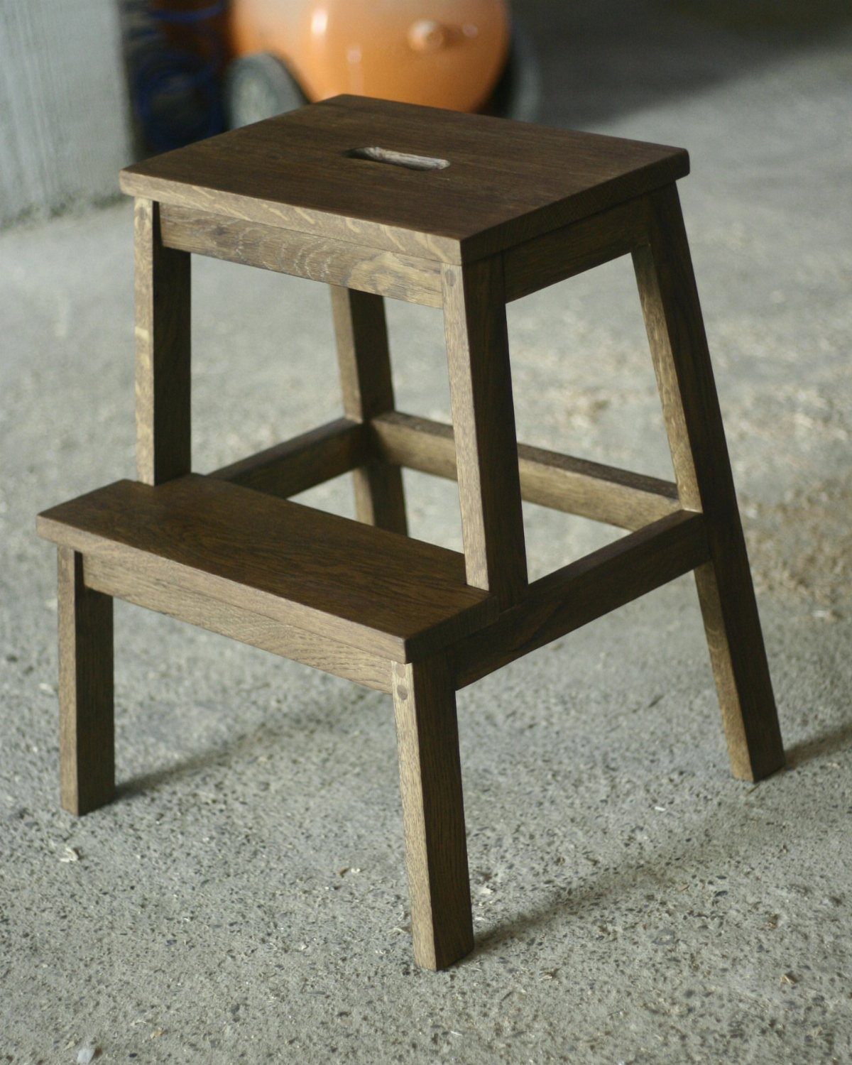 Dark brown wooden two-step stool standing on a grey concrete floor.