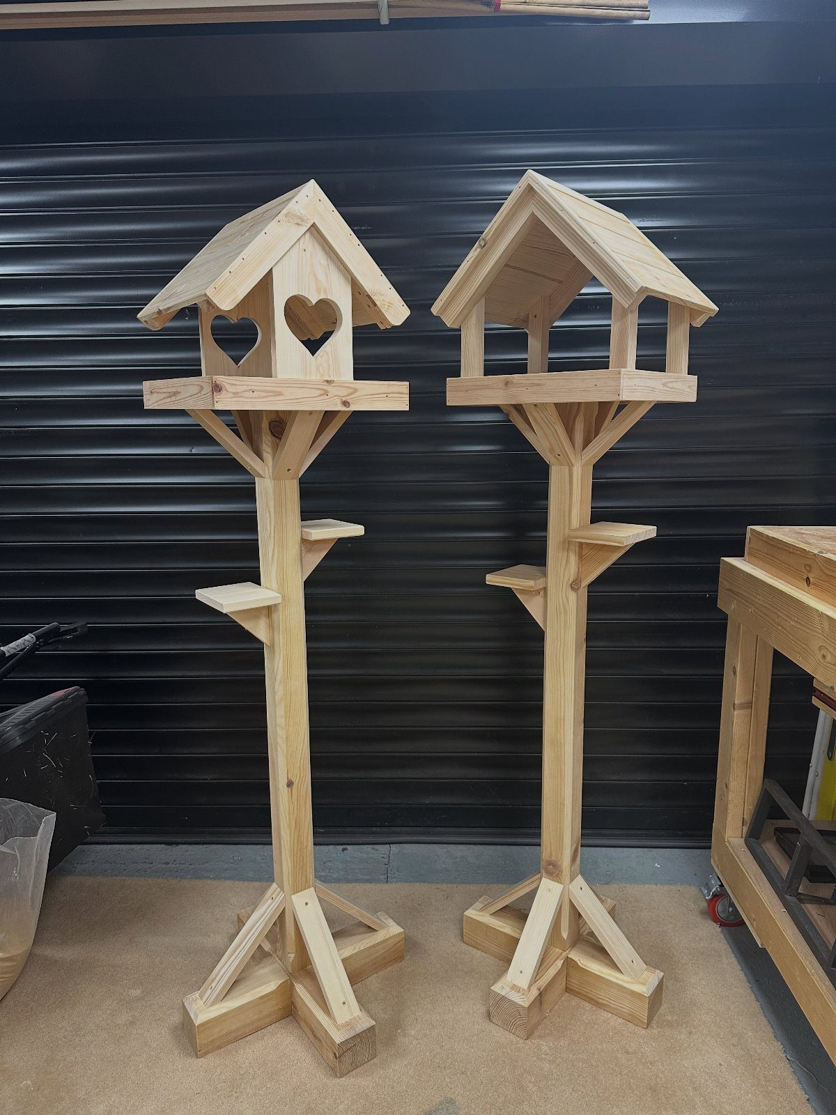 Two tall wooden birdhouses on poles with peaked roofs and heart-shaped entrance.