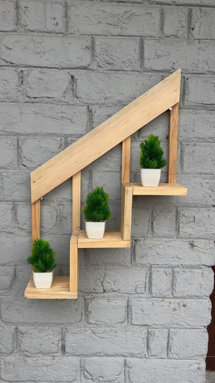 Wooden house-shaped wall shelf holding three small potted green plants on a brick wall.