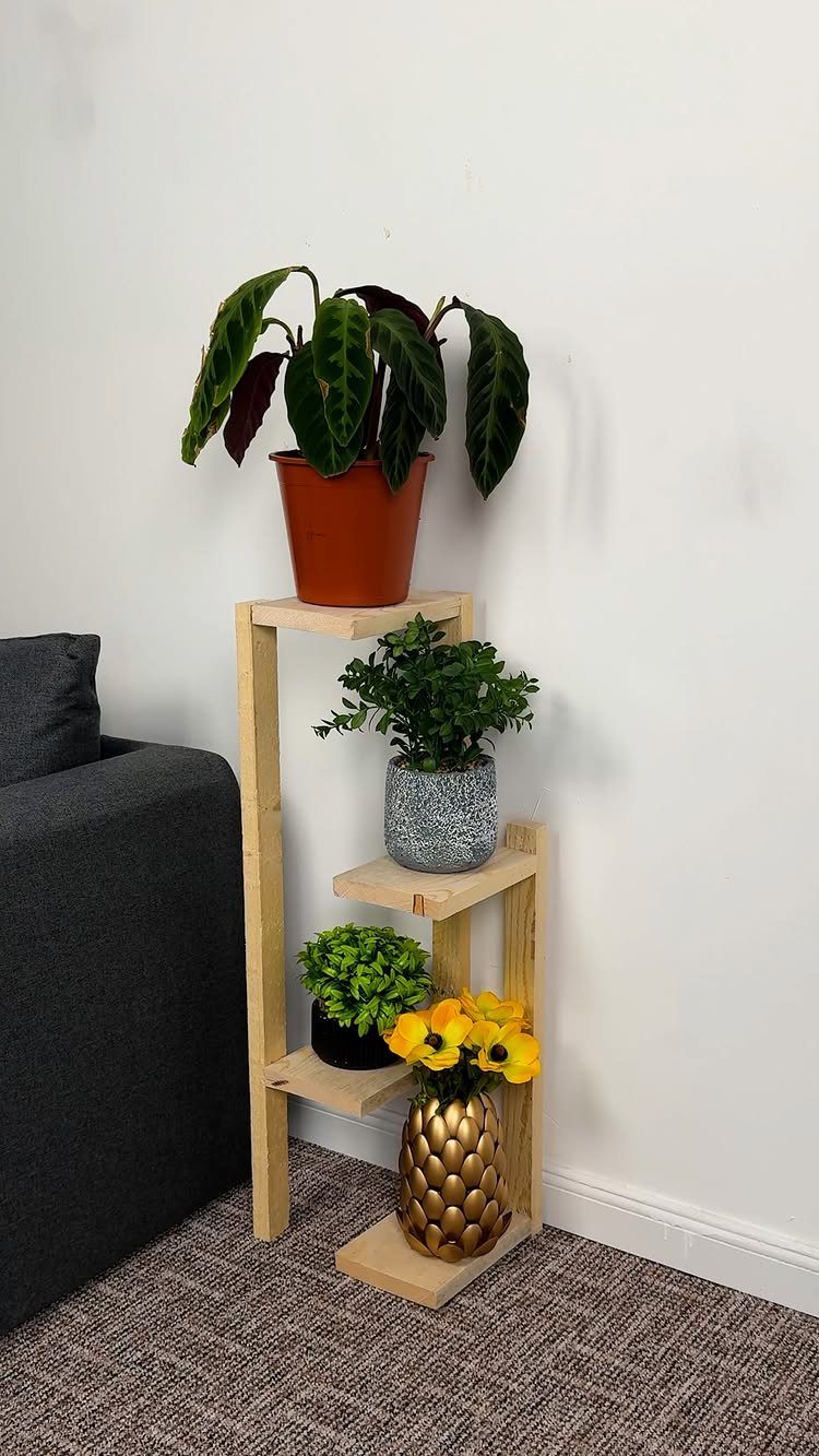 Tiered light wood plant stand holding various potted indoor plants and yellow flowers.