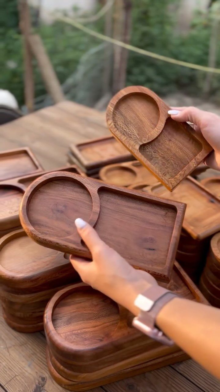 Wooden serving trays with circular and rectangular sections held by a person's hands.