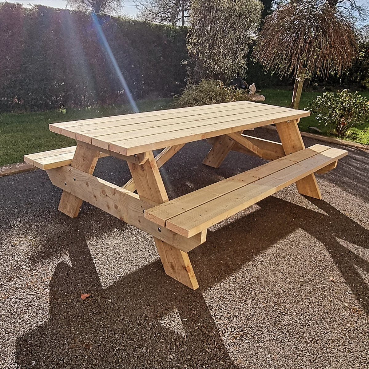 Wooden picnic table with attached benches on a gravel patio in a garden.