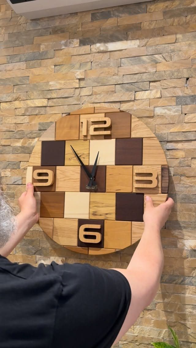 Circular wooden wall clock with mosaic squares and carved numbers on stone wall.