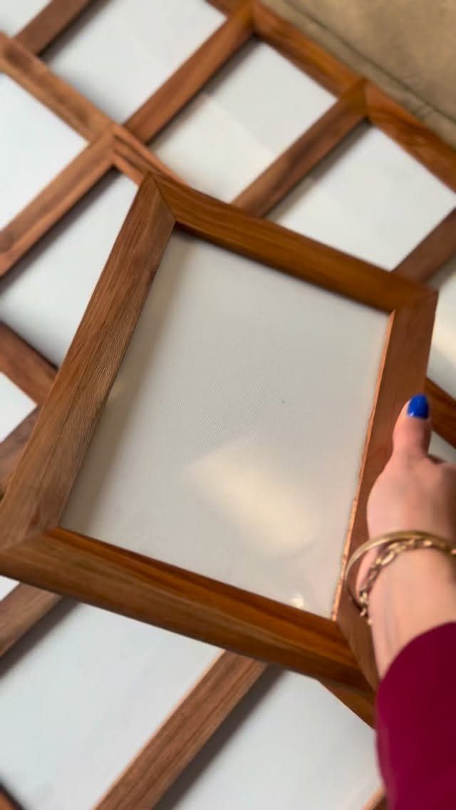 Square wooden picture frame with glass held by a hand with blue nails.