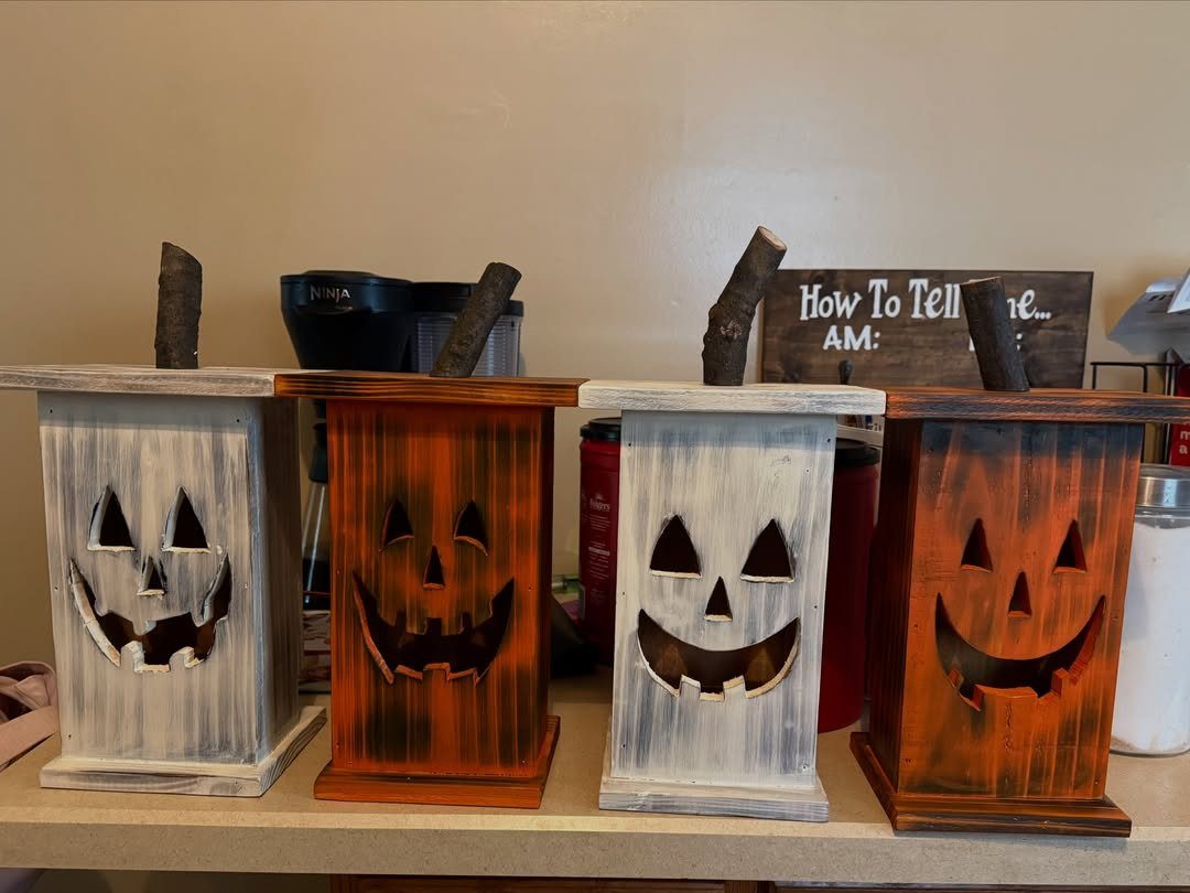 Four wooden jack-o'-lantern lanterns in white and orange colors on a countertop.