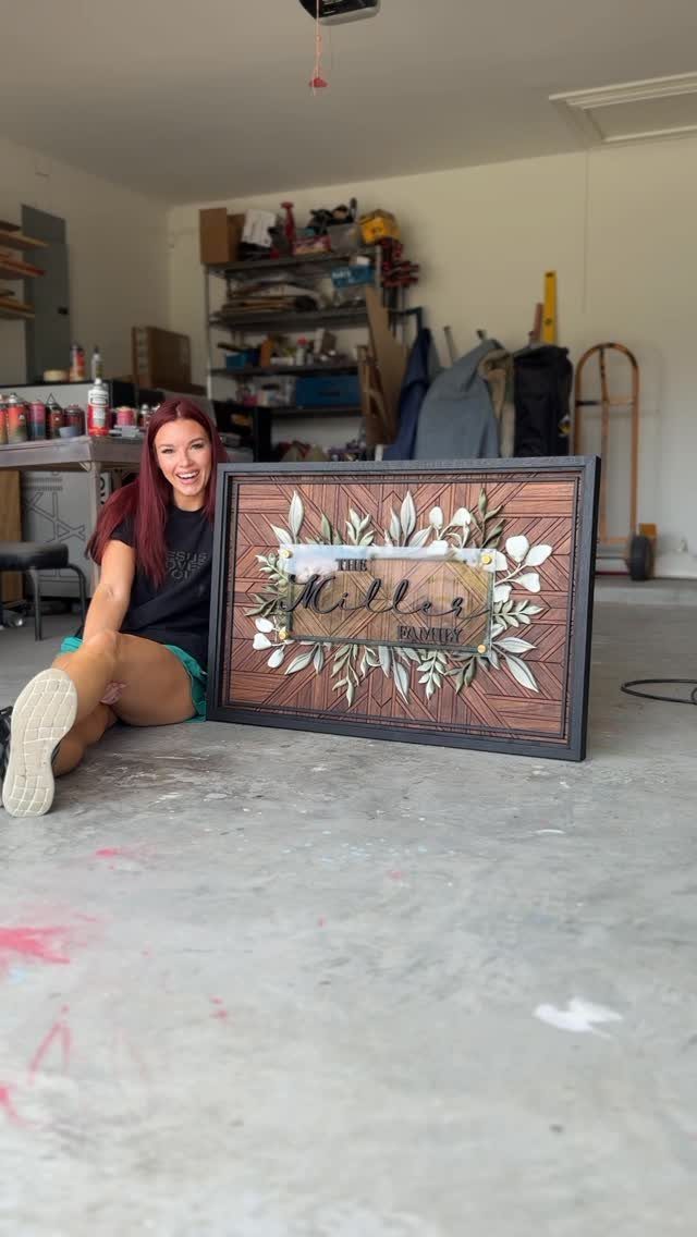 Woman sitting next to a large rectangular wooden wall art piece with floral carvings.