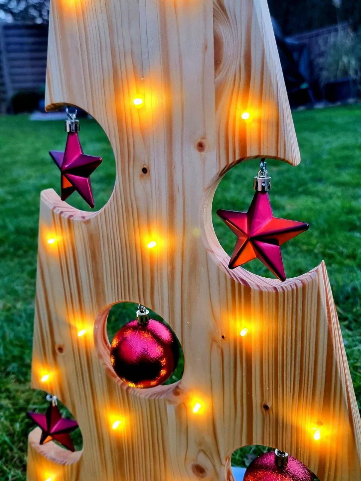 Wooden decorative structure with red ornaments and glowing yellow fairy lights on grass