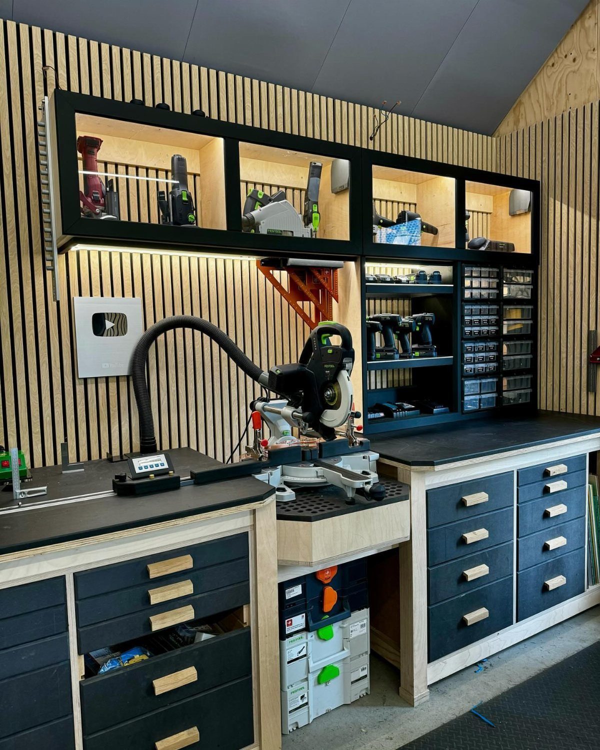 8 Woodshop Design Ideas for Smarter Storage and Layout 6 Modern woodshop workstation with black drawers, miter saw, and illuminated wall storage cabinets.