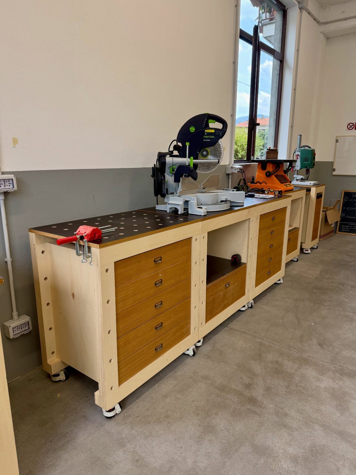 8 Woodshop Design Ideas for Smarter Storage and Layout 4 Wooden workbench with drawers and a miter saw on wheels in a workshop.