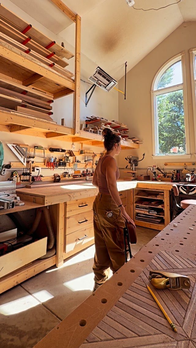 8 Woodshop Design Ideas for Smarter Storage and Layout 2 Woman in a woodshop with overhead lumber storage racks and wooden workbenches.