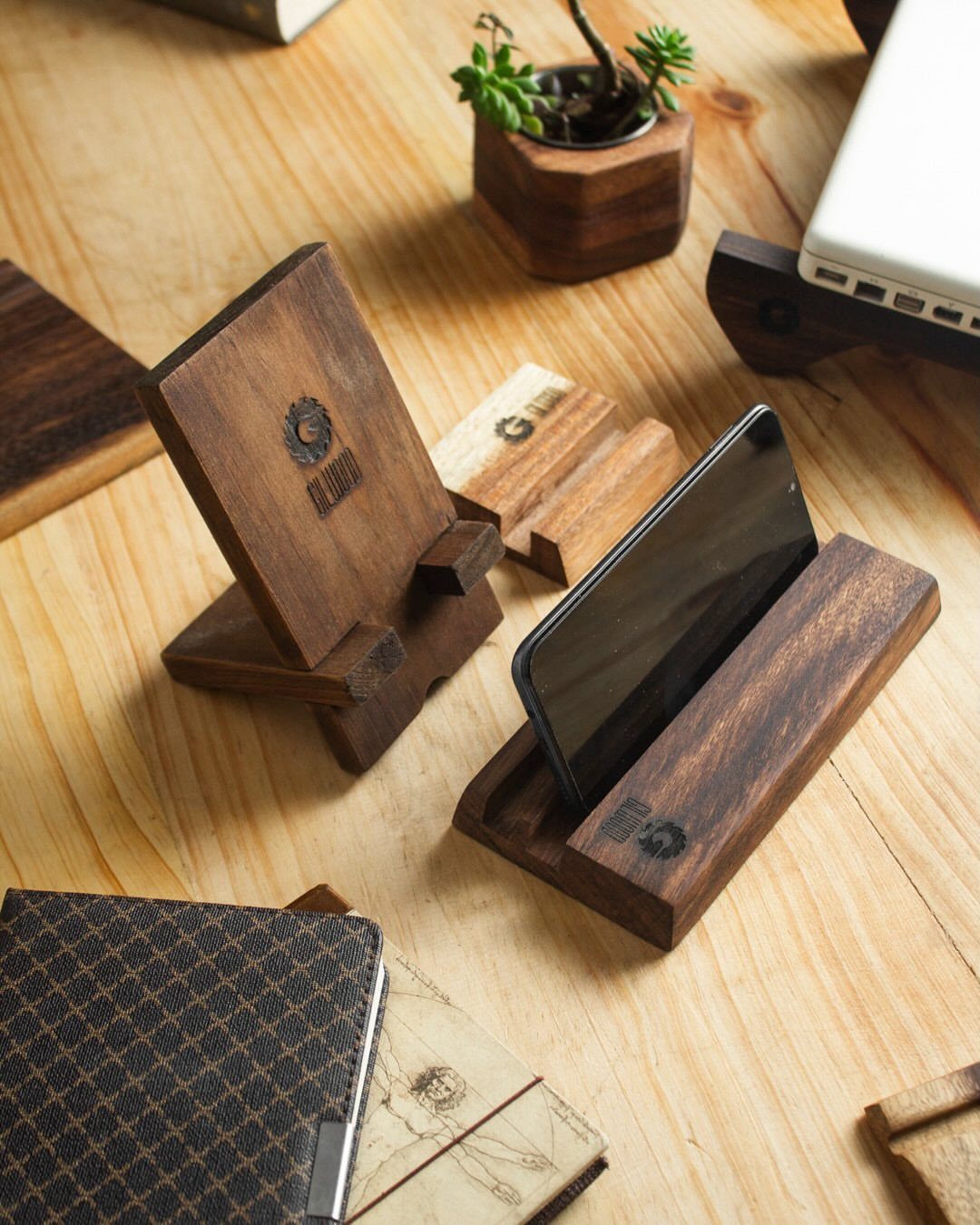 Wooden phone and tablet stands resting on a light-colored wooden desk surface.
