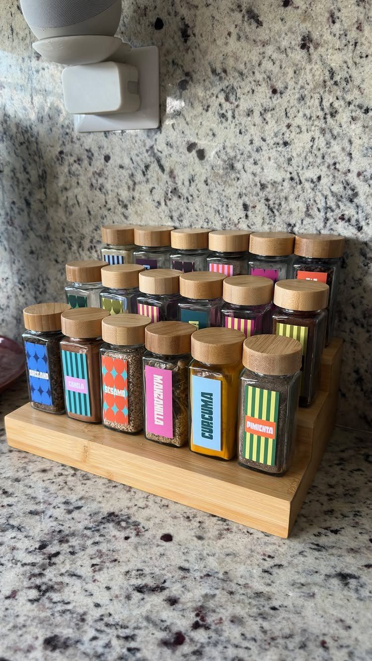 Wooden spice rack holding small glass jars with colorful labels on a granite counter.