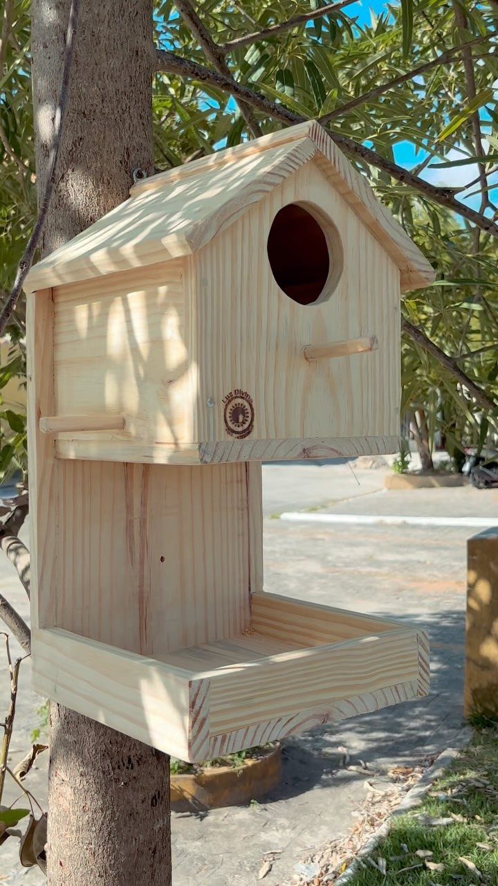 Wooden birdhouse with a feeding tray mounted on a tree trunk in a garden.