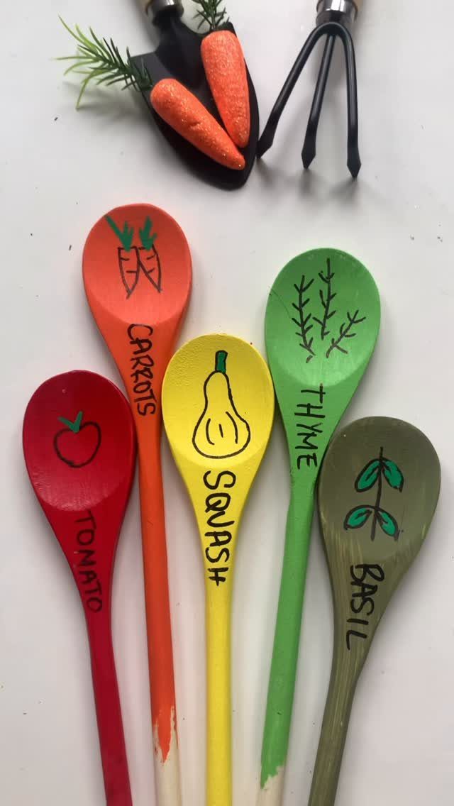 Colorful painted wooden spoons used as garden markers for tomato, carrots, squash, thyme, and basil.