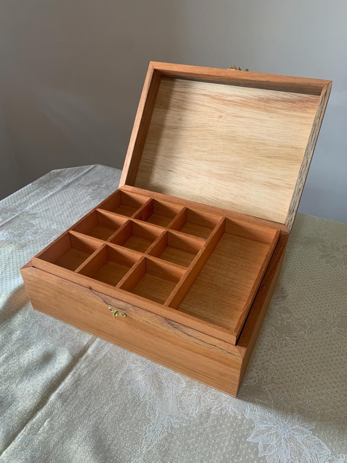 Wooden jewelry box with a divided storage tray and open lid on fabric.