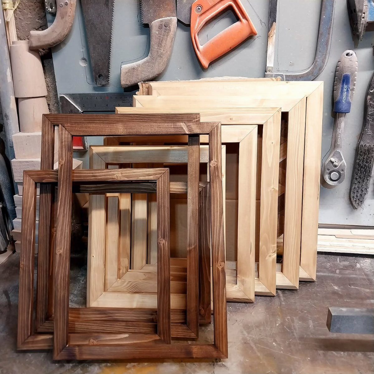 Wooden picture frames in different sizes and stains leaning in a woodworking shop.