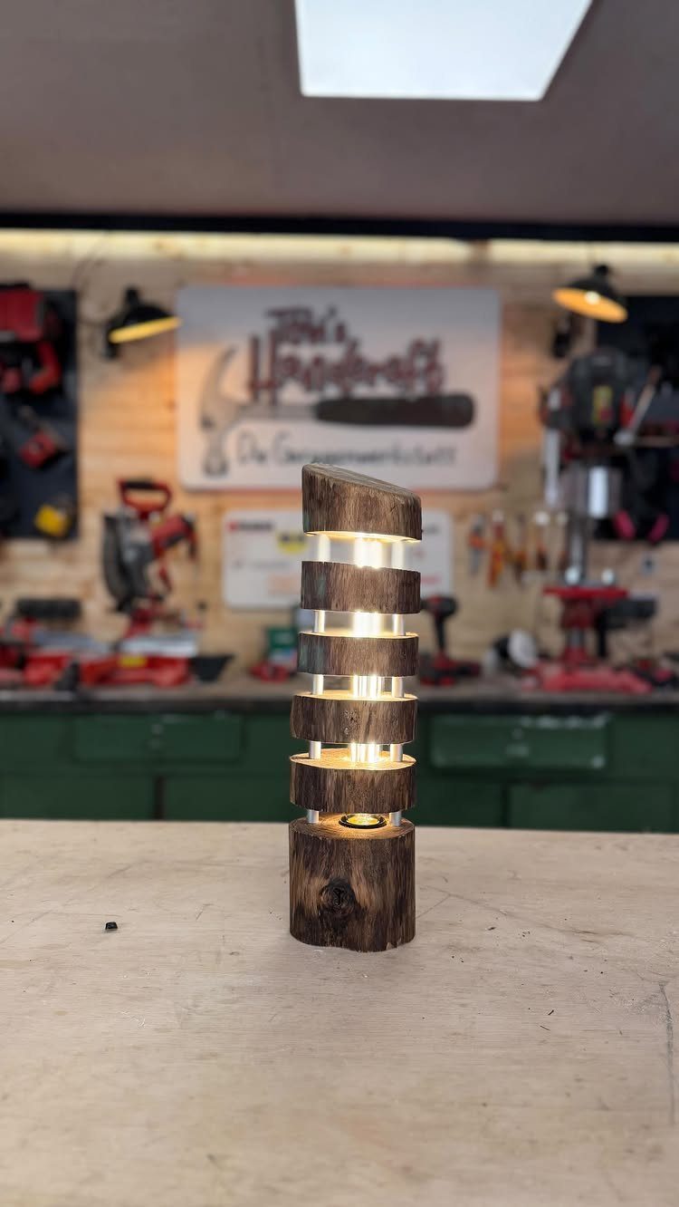 Wooden lamp made of stacked carved slices glowing on a workshop workbench.