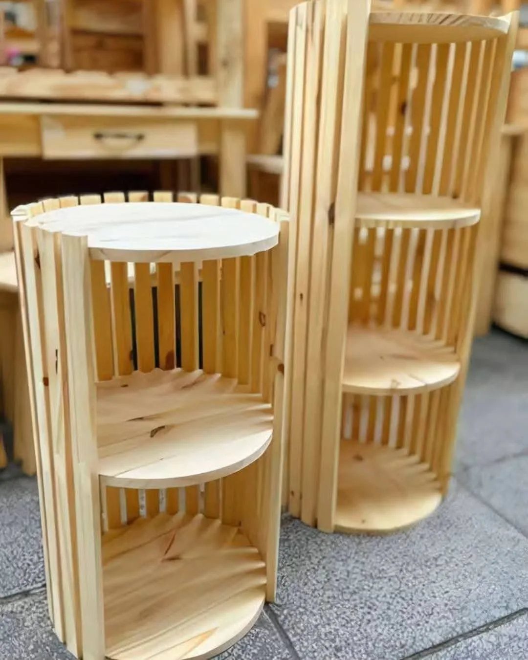 Two light wood circular shelving units with vertical slats in a workshop setting.