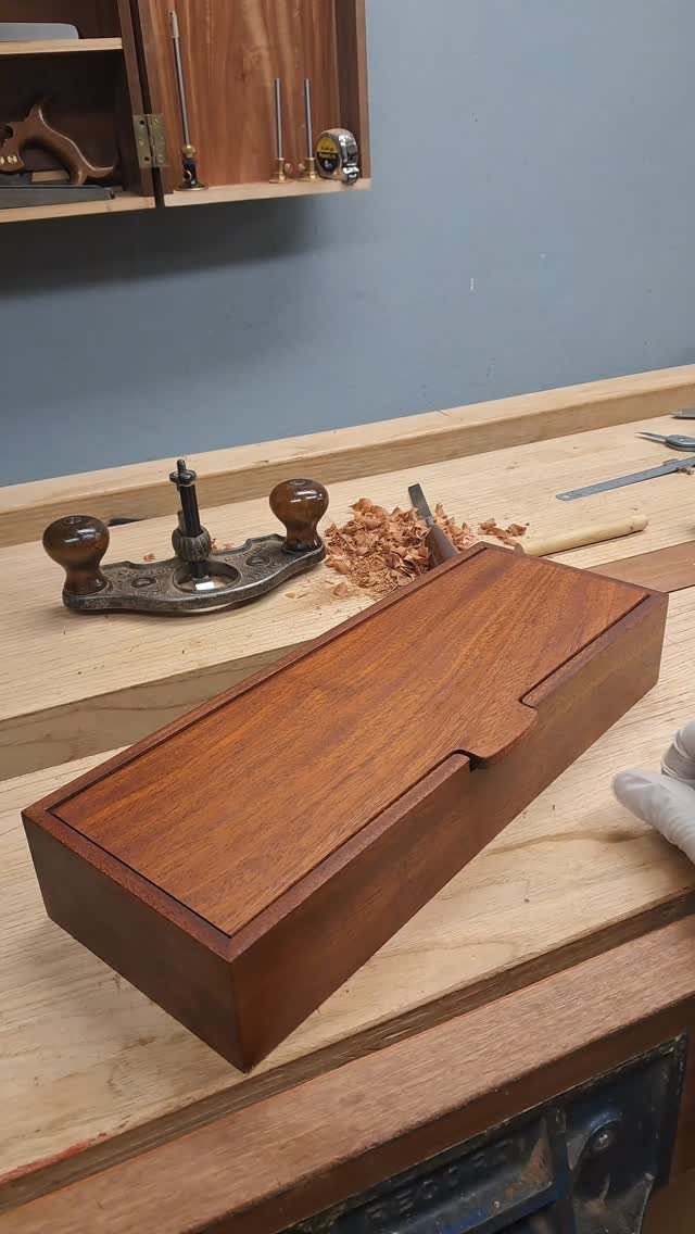 Polished brown wooden box with a lid resting on a woodworking workbench
